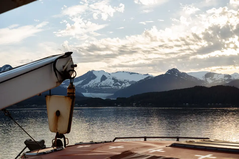 White boat crane over a channel toward snow mountains and a glacier near Juneau
