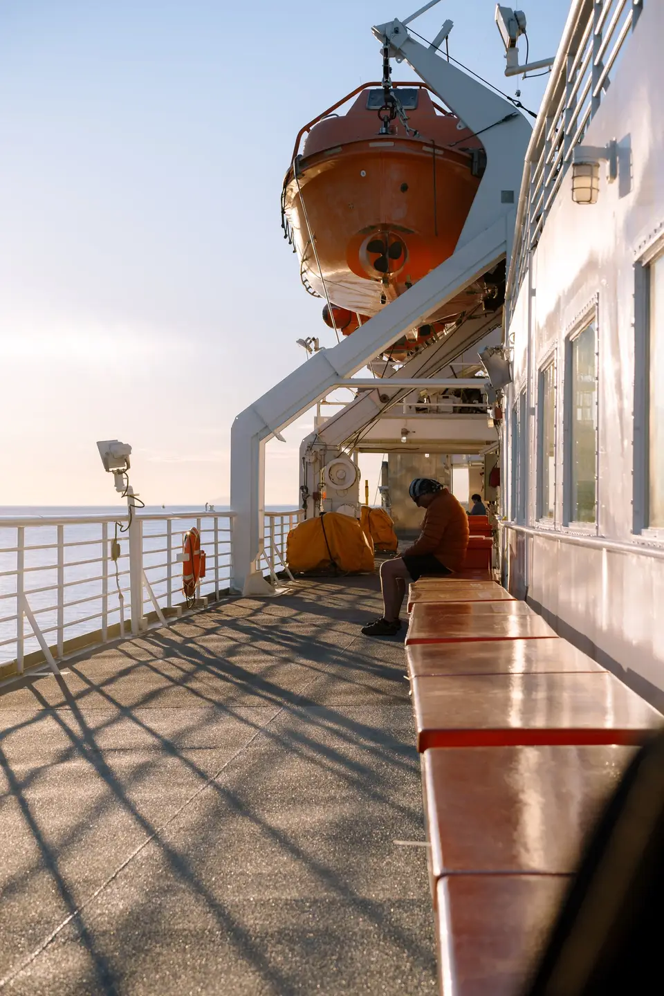 A passenger on orange ferry benches at sunset, life raft overhead, near Ketchikan, Alaska