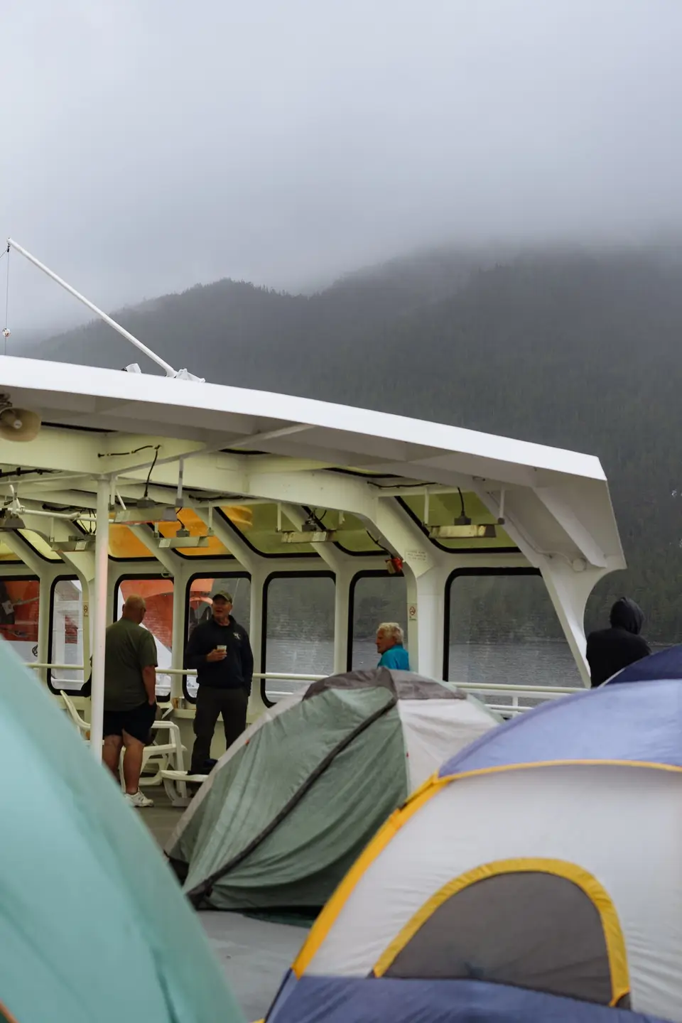 Three men stand under the solarium heat lamps of the MV Matanuska while rain and fog fall outside somewhere between Bellingham, WA and Ketchikan, AK