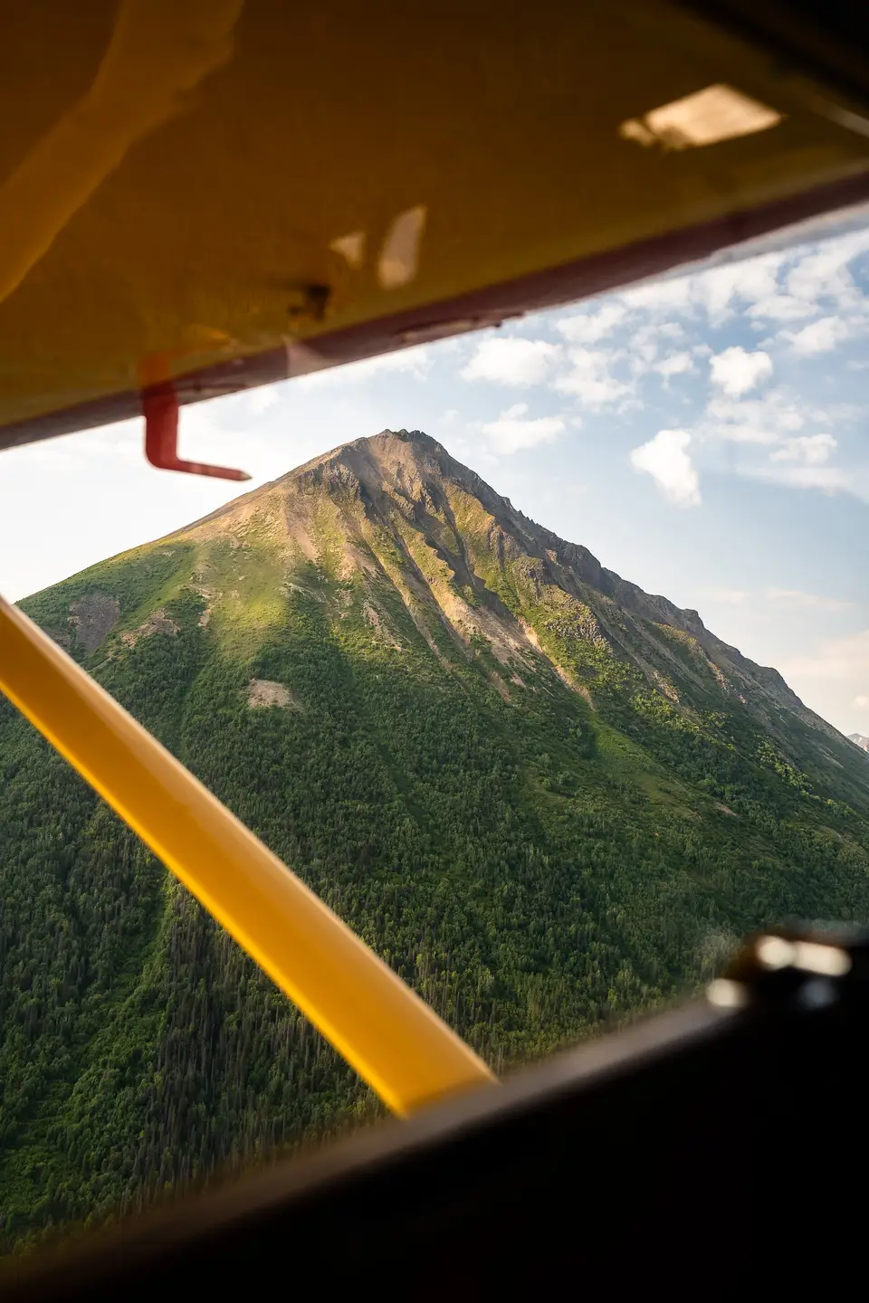 A green, pointed peak framed by a yellow plane strut over Wrangell–St. Elias, Alaska