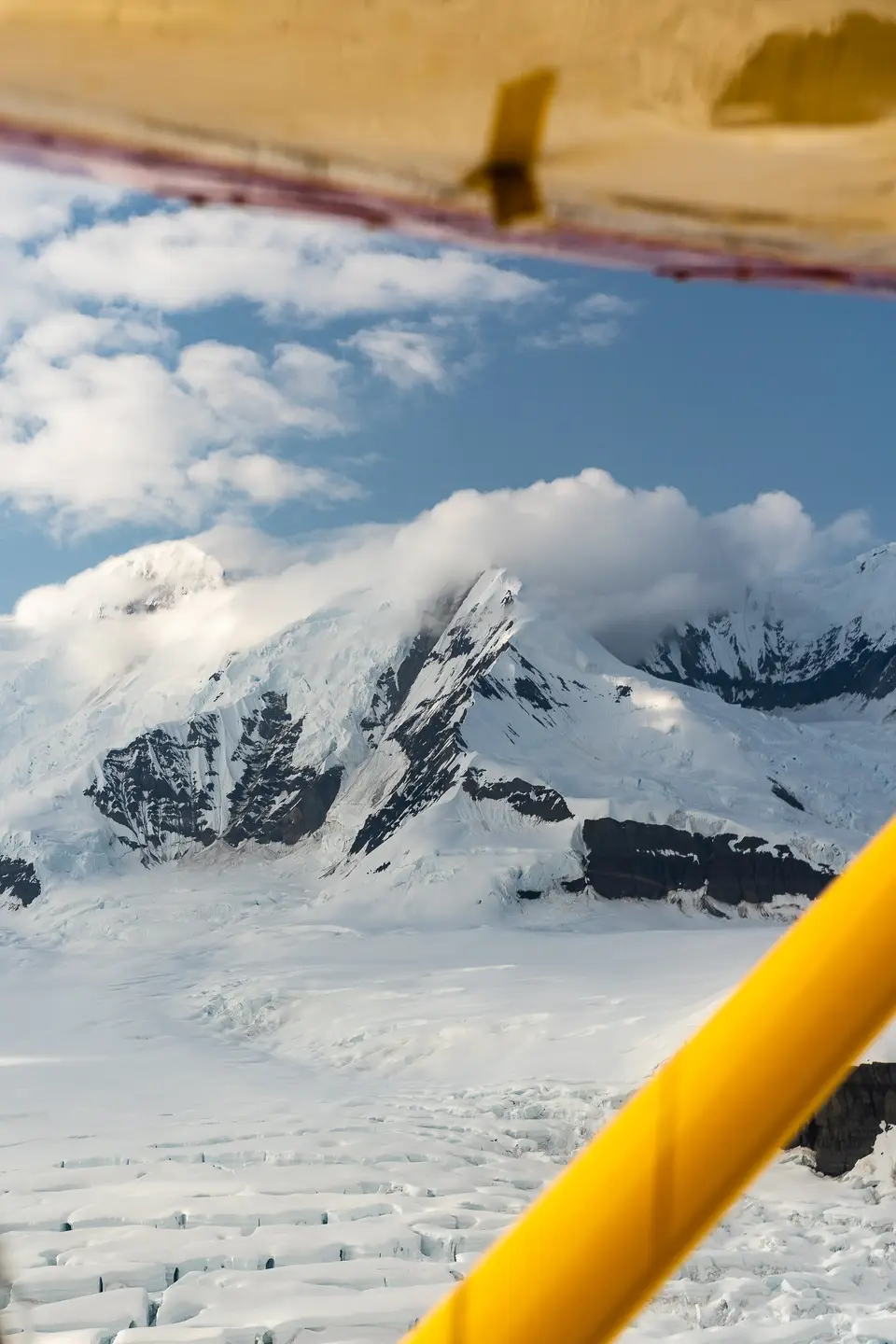 A snow peak and crevassed glacier past a yellow plane strut over Wrangell–St. Elias, Alaska