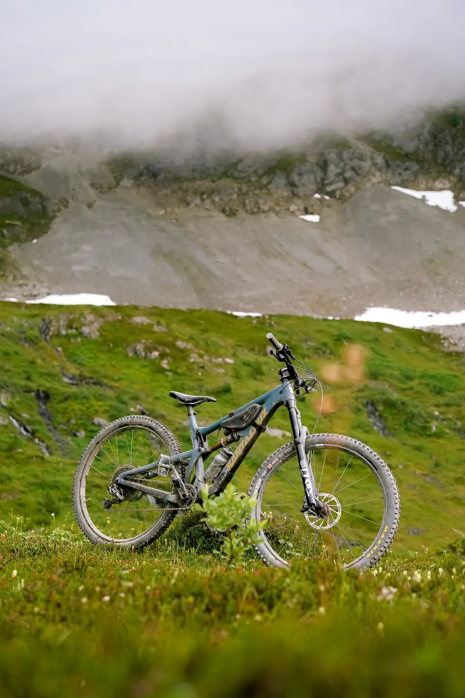 A mountain bike standing in green grass below misted slopes near Alyeska, Alaska