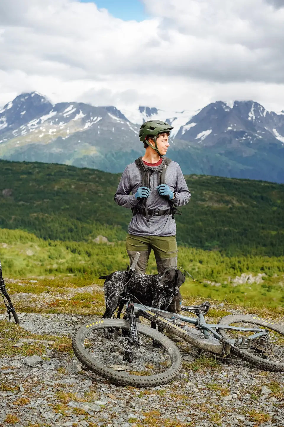 A rider standing with Penelope and two mountain bikes, snow-streaked peaks behind, near Seward, Alaska