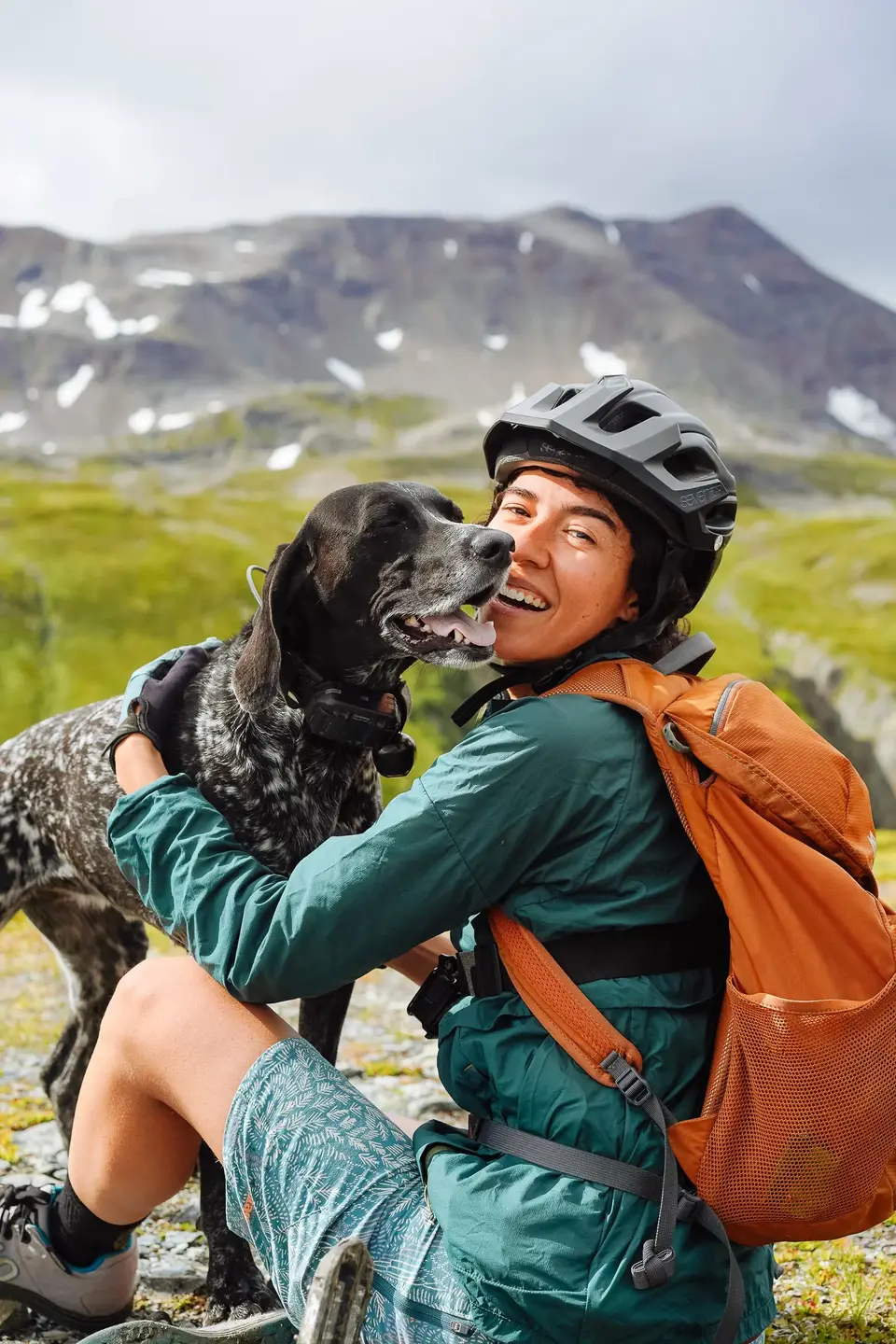 A rider in a helmet and orange pack getting a kiss from Penelope near Seward, Alaska