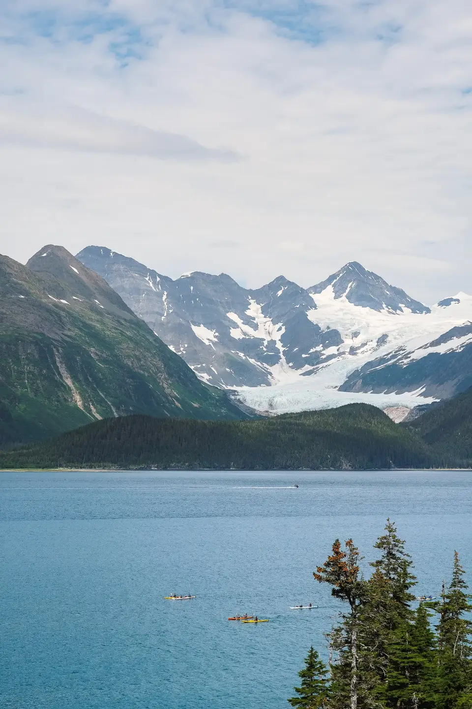 A bright blue bay below snow-dusted peaks and a glacier near Whittier, Alaska