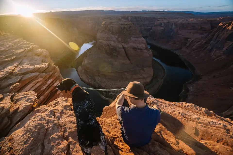 Dog and person sitting on edge of Horseshoe Bend at sunset