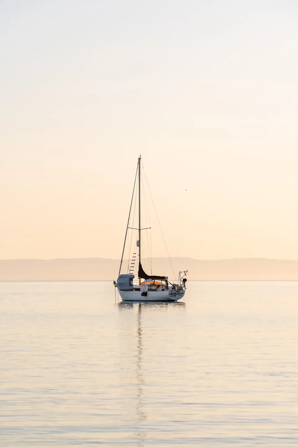 A white sailboat anchored on glassy water at dawn near La Paz, Baja California Sur