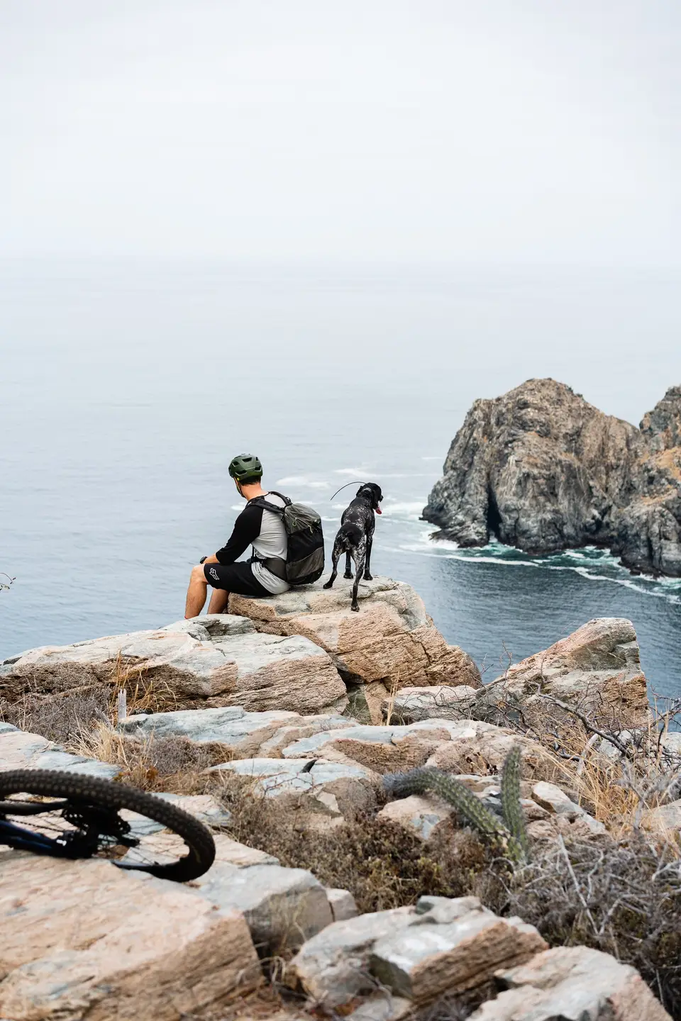 A person sitting on a pale cliff edge looking out to a hazy sea near Todos Santos, Baja California Sur