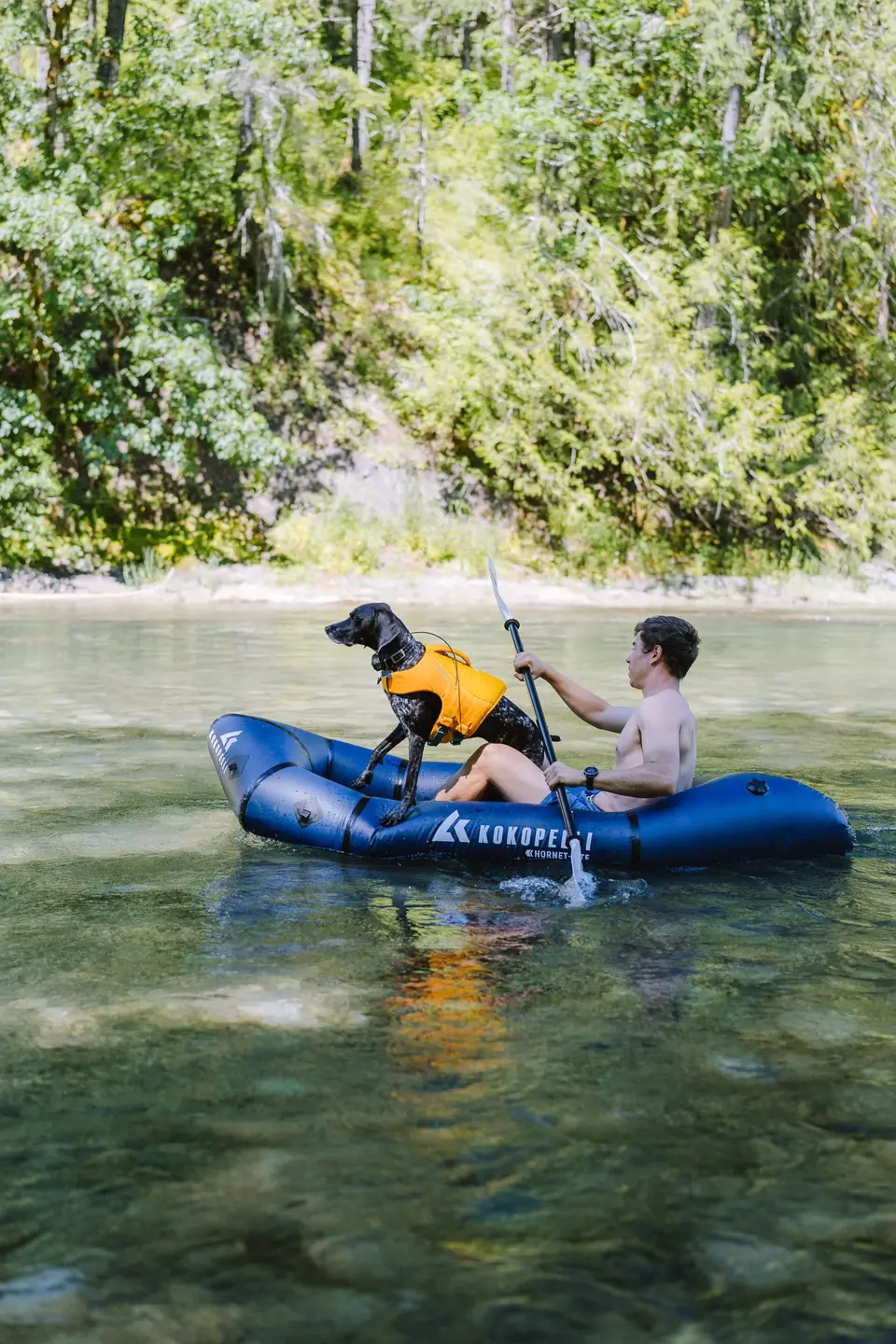 Evan paddling a blue Kokopelli packraft with Penelope in an orange life vest on the Cowichan River, Vancouver Island