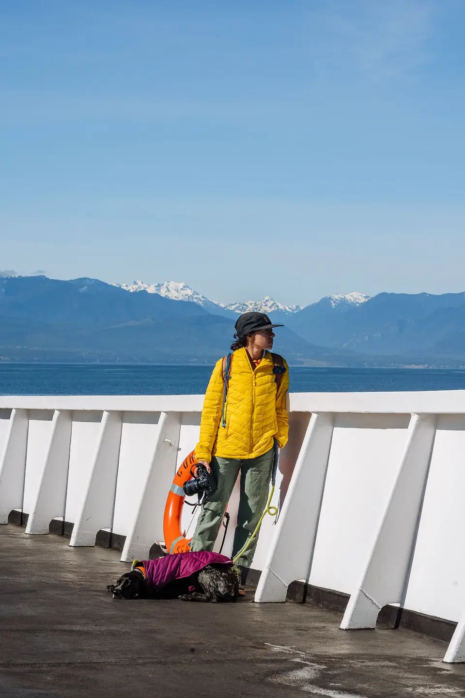 Melanny in a yellow jacket on the ferry deck, Penelope at her feet