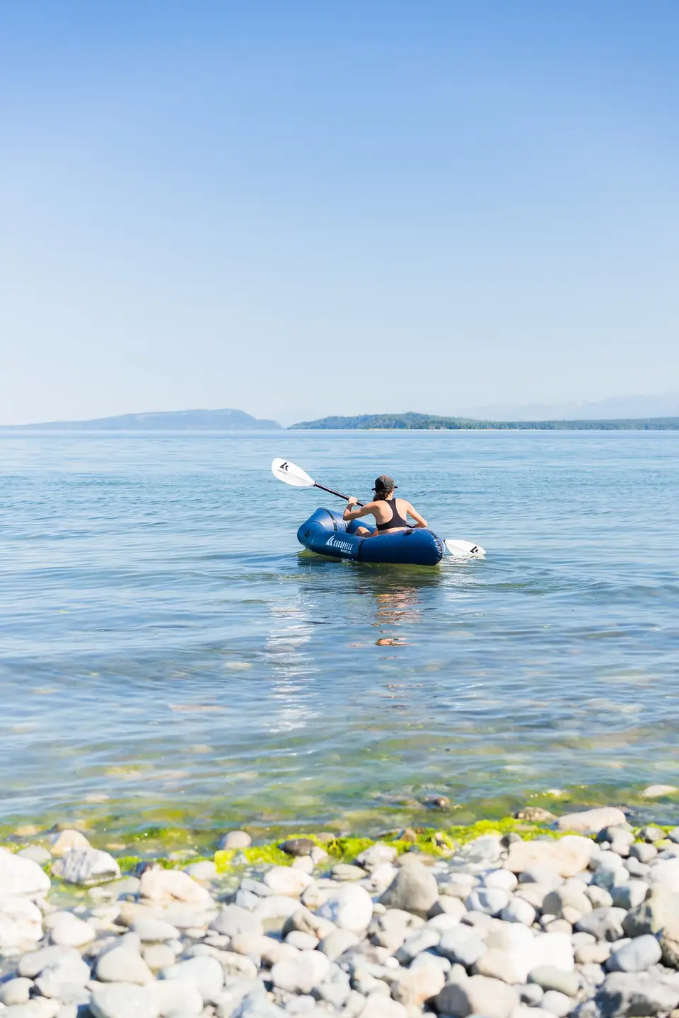 A blue packraft on calm open water off a pebble shore in the Comox Valley, Vancouver Island