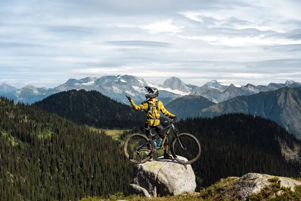 A rider on a ledge above forest and snow peaks near Revelstoke, British Columbia