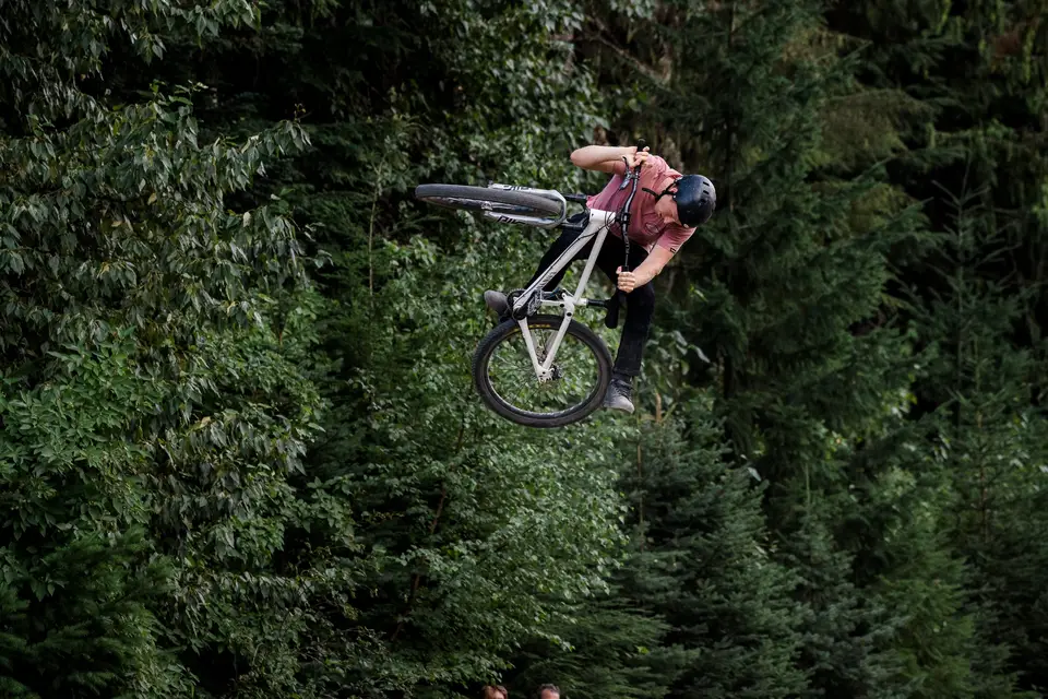 A mountain biker whipping a jump in front of dense forest in Whistler, British Columbia
