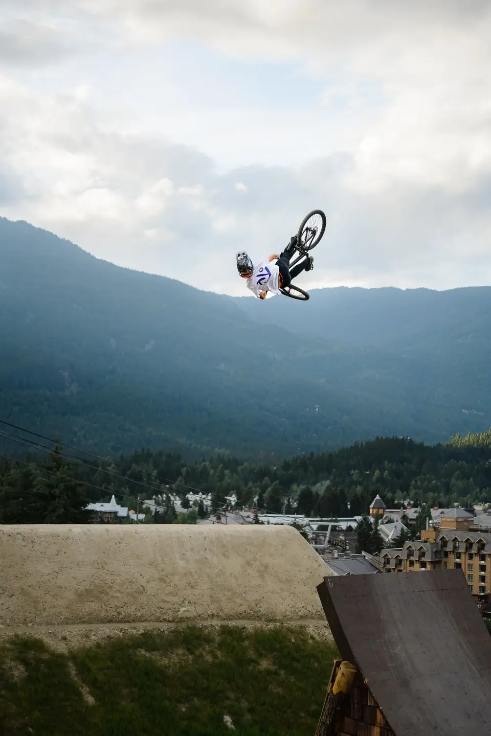 A mountain biker upside down in a backflip above the valley and town in Whistler, British Columbia