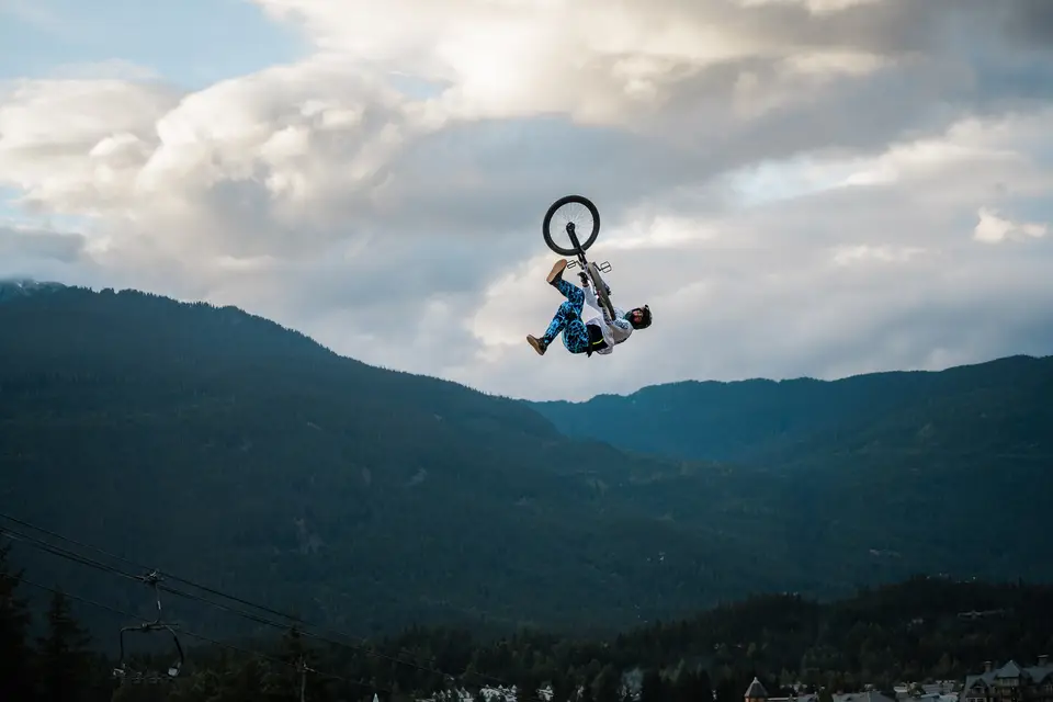 A mountain biker mid-backflip above evergreen hills in Whistler, British Columbia