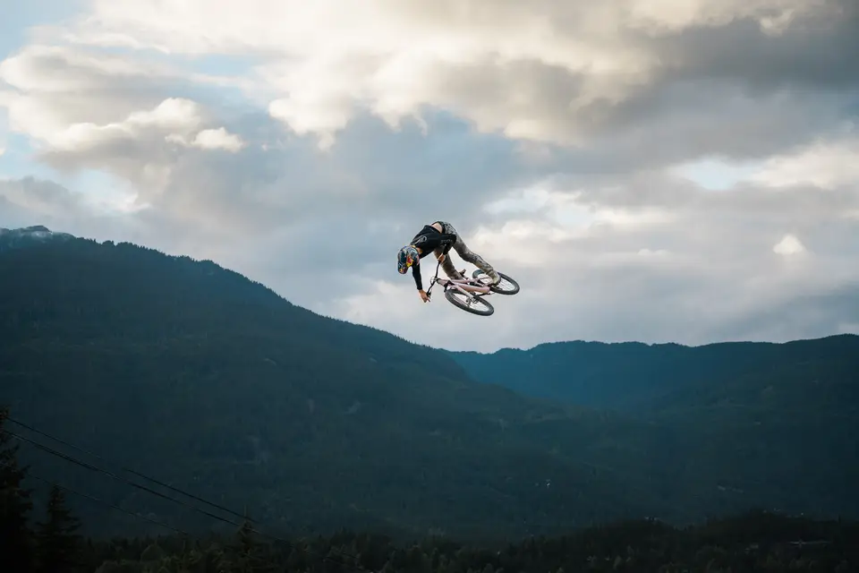 A mountain biker in the air, silhouetted against clouds above dark ridges in Whistler, British Columbia