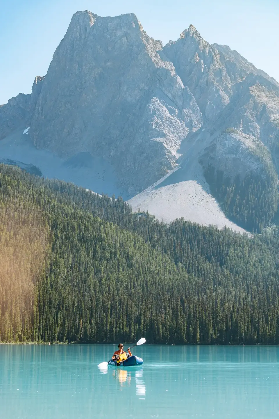 A packrafter in an orange shirt on turquoise water below a grey peak near Banff, Alberta