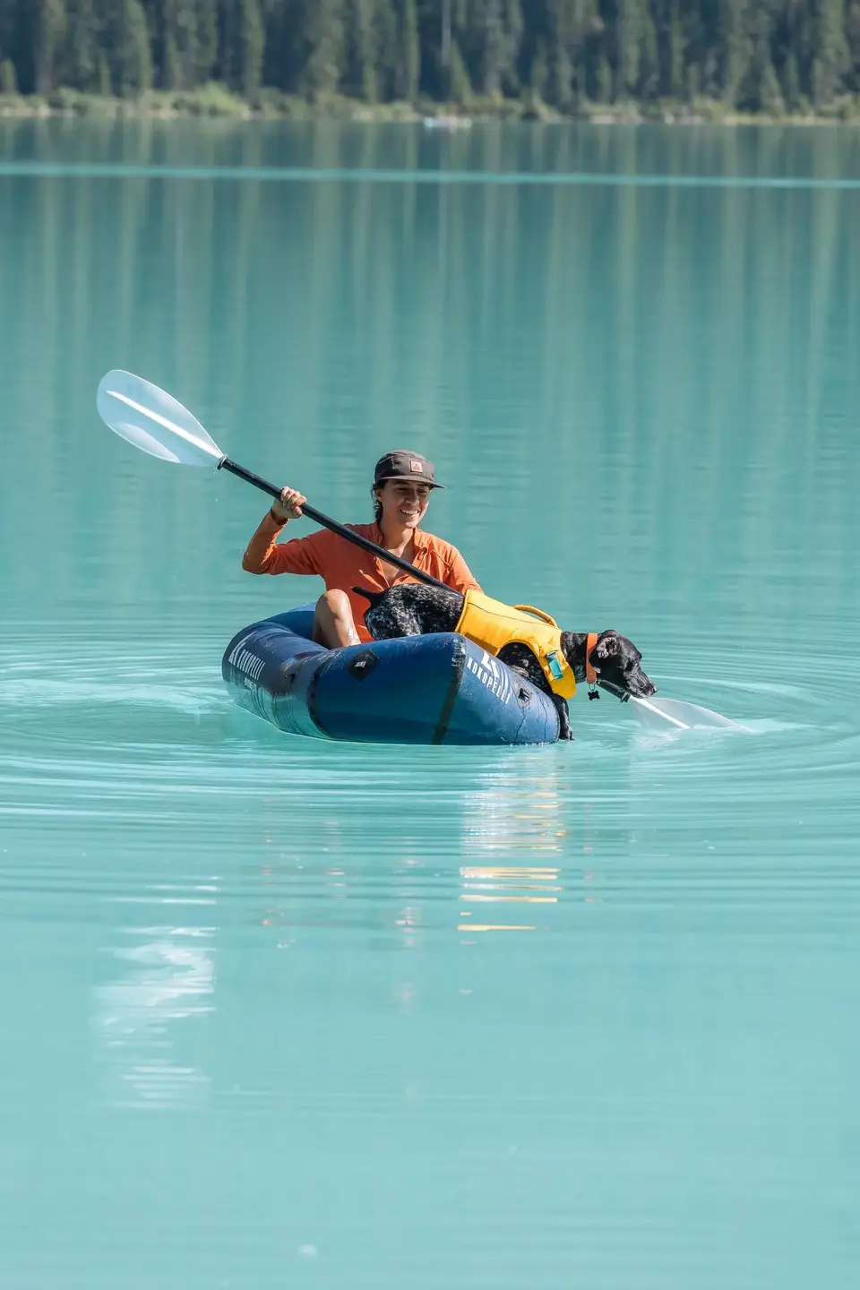 A packraft on bright turquoise water with a dog at the bow near Banff, Alberta