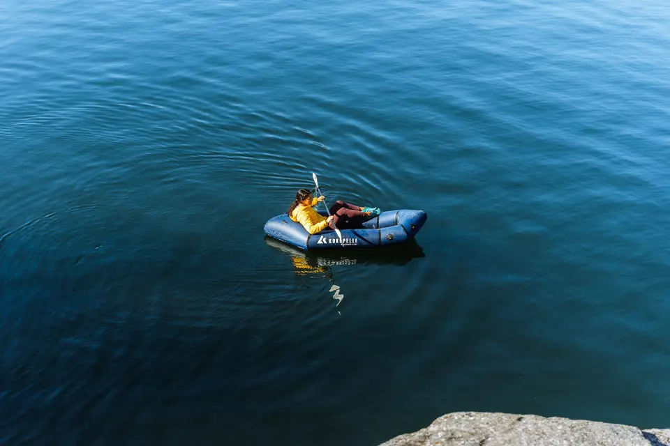Overhead view of a paddler and a dog in a blue packraft on deep blue water near Cranbrook, British Columbia
