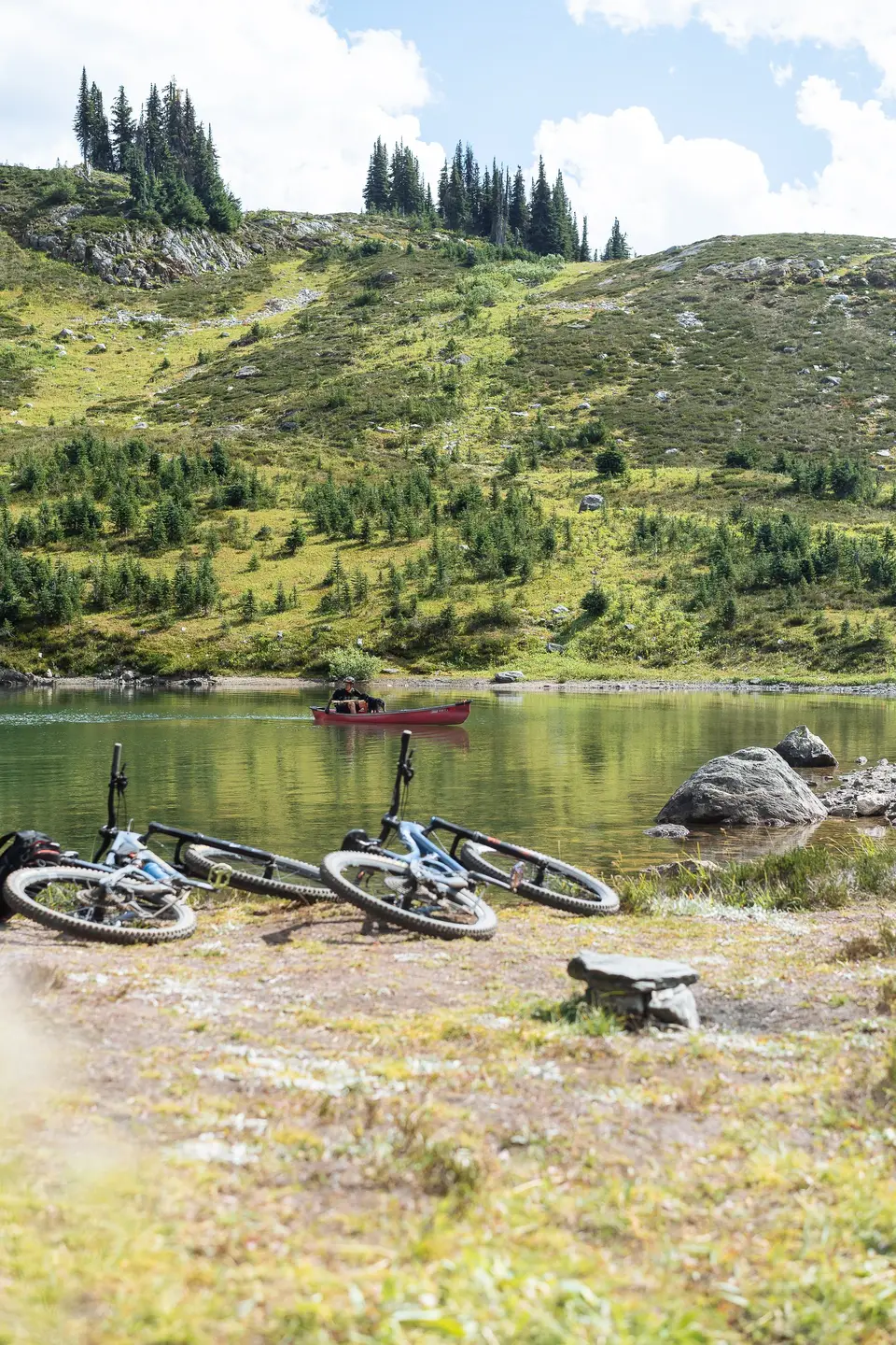 Mountain bikes lying on the shore of an alpine lake, a small red boat on the water, in Revelstoke, British Columbia