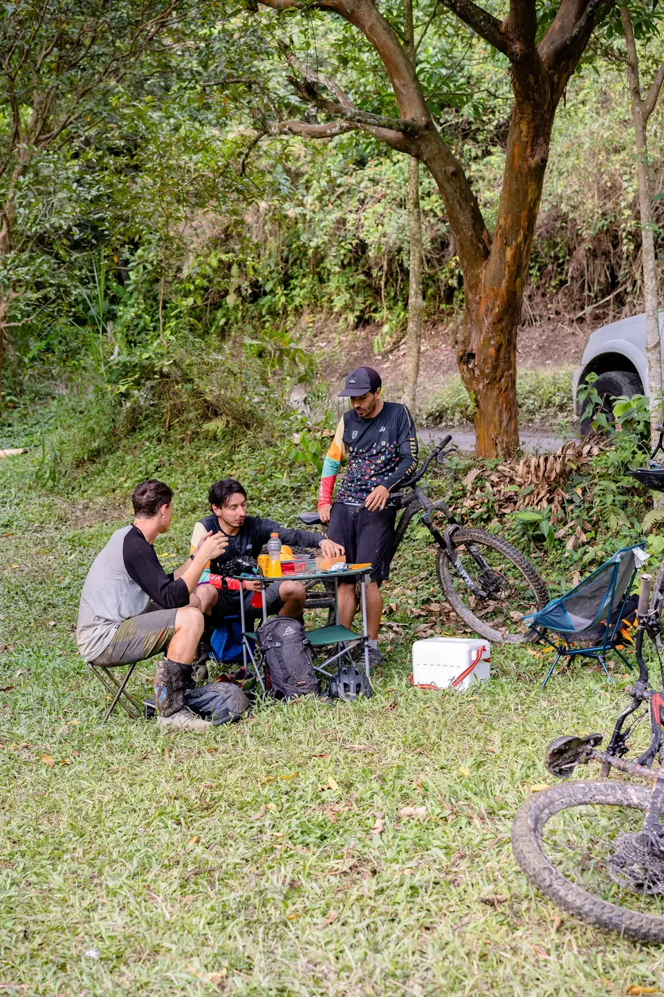 Four people at a small table in the shade, bikes against a tree, in rural Colombia