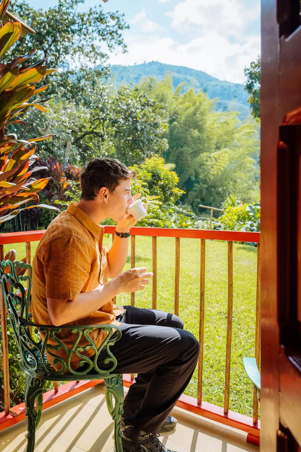 Evan on a red-railed balcony with a mug, green valley behind him, in Colombia