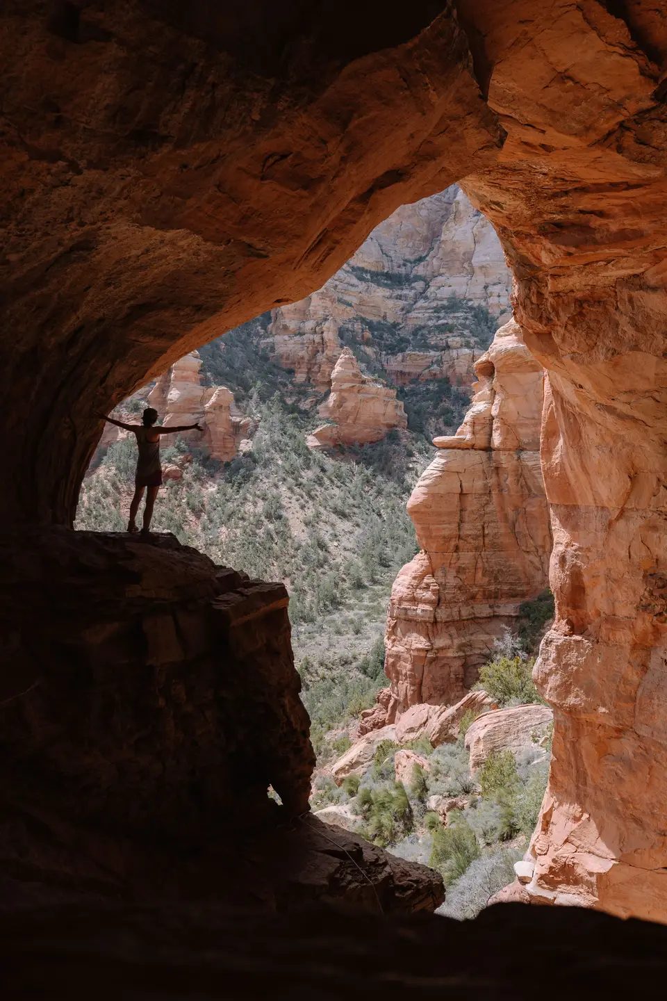 A person standing inside a rock cave with arms outstretched in Sedona