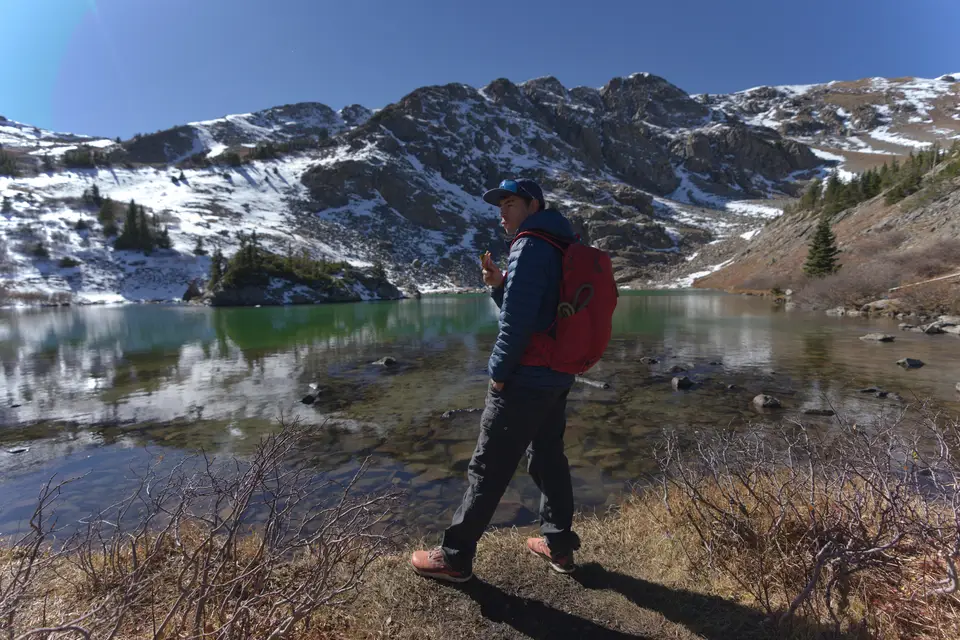 Hiking along a green alpine lake below snowy peaks near Cottonwood Pass, Colorado