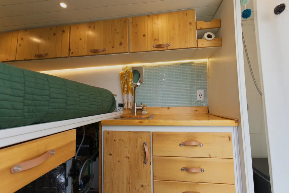 Wood kitchen counter and cabinets with a sea glass backsplash inside our van