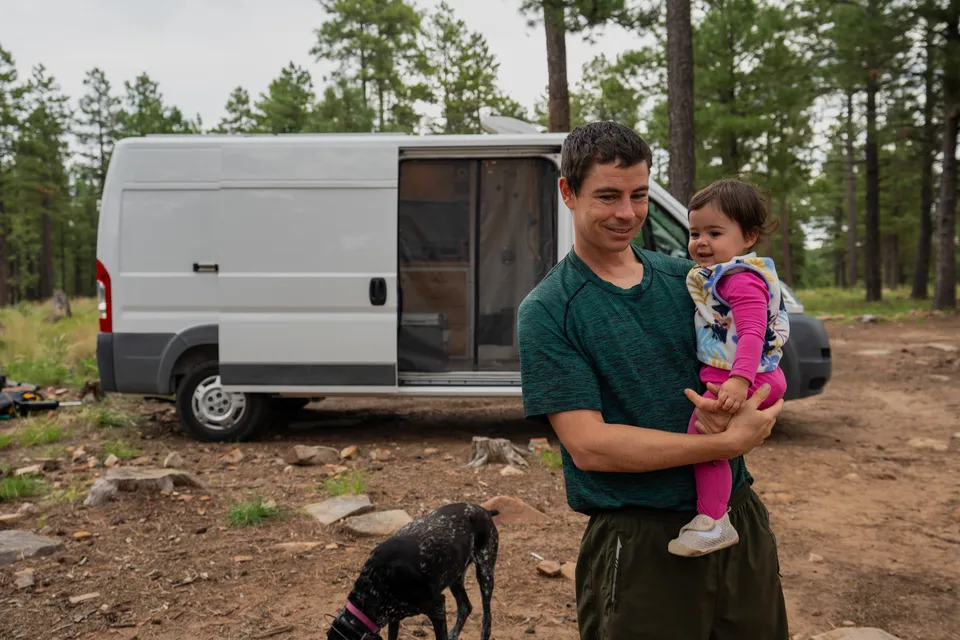 Evan holding Mia at camp with Penelope at his feet and our van behind them