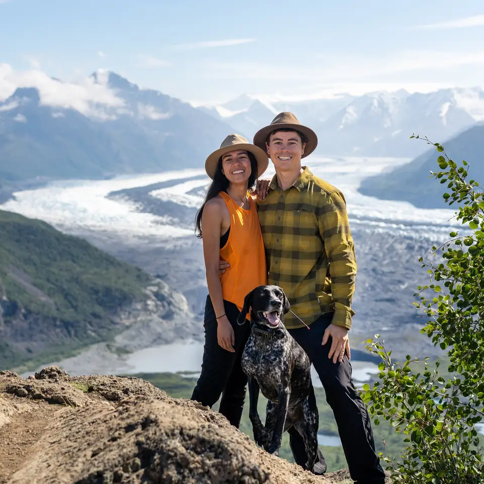 A couple and their dog hiking in a mountainous area with glaciers